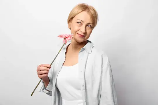 Светловолосая женщина с розовым цветком у лица на сером фоне
