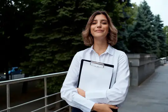 Уверенная женщина с планшетом в руках на улице среди деревьев