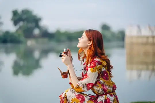 Рыжеволосая девушка с пленочным фотоаппаратом у реки