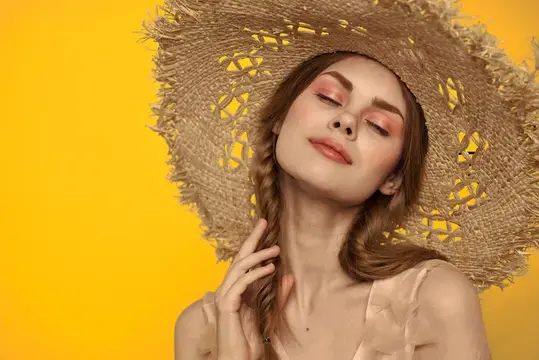 Молодая женщина в соломенной шляпе с закрытыми глазами на жёлтом фоне