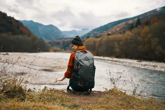 Женщина-туристка с рюкзаком путешествует, идёт по реке в горном пейзаже