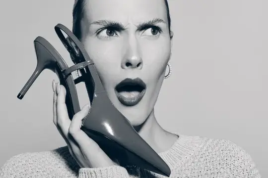 Удивлённая женщина с туфлей на шпильке у лица