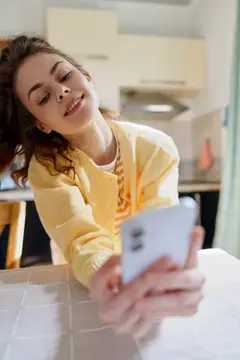 Улыбающаяся девушка с телефоном лежит на столе на светлой кухне