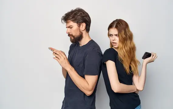 Мужчина и женщина стоят спиной к спине, глядя в телефоны с недовольством