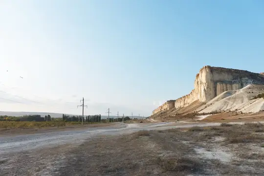 Живописная проселочная дорога с горами вдалеке и линиями электропередач, протянувшимися через открытое поле