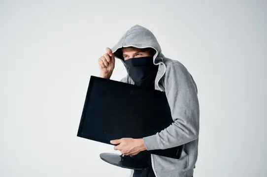 Мужчина в капюшоне и маске крадёт монитор на светлом фоне
