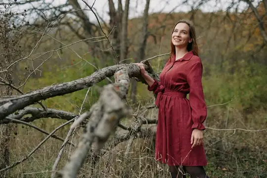 Улыбающаяся девушка в бордовом платье у сухого дерева в осеннем лесу