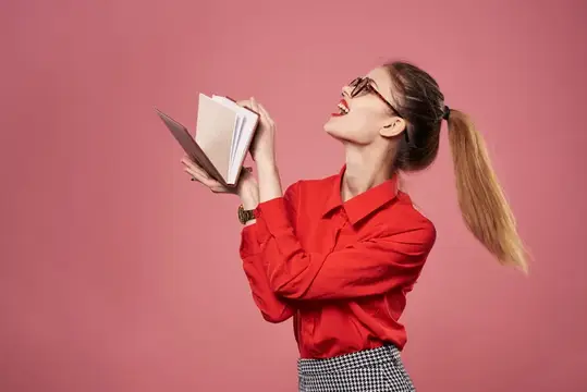 Девушка в красной рубашке радостно читает книгу на розовом фоне