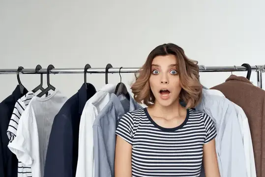 Удивлённая девушка перед вешалкой с одеждой