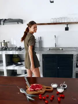 Молодая женщина на кухне с мясом и специями на столе