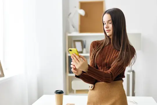 Молодая женщина с длинными волосами смотрит в смартфон в светлом офисе