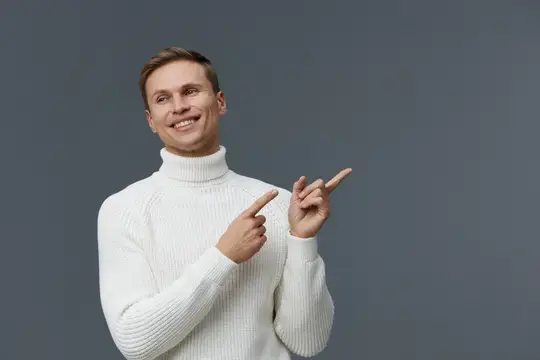 Улыбающийся мужчина в белом свитере показывает пальцами в сторону