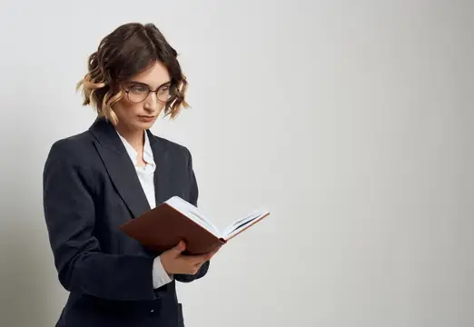 Деловая женщина в очках сосредоточенно читает книгу на светлом фоне