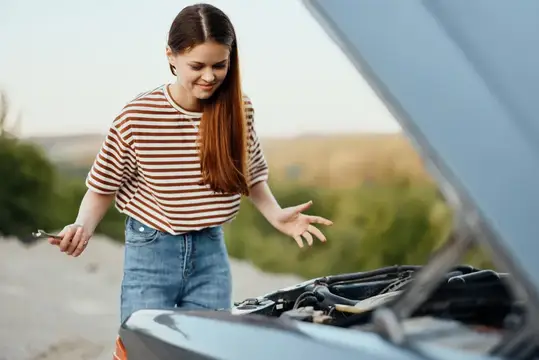 Девушка с гаечным ключом смотрит на открытый капот автомобиля
