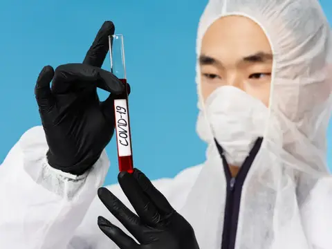 Медик в защитном костюме держит пробирку с анализом на COVID-19