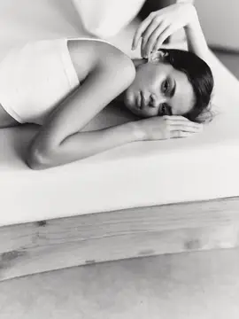 Молодая темноволосая женщина лежит на белой кровати в задумчивости