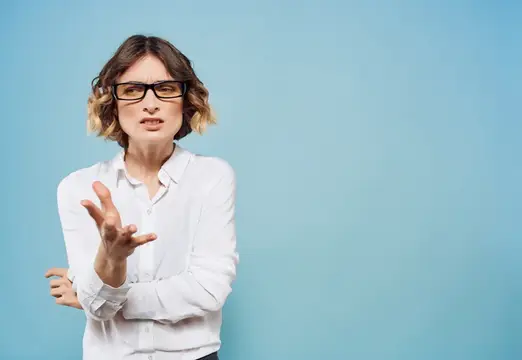 Женщина в очках и белой рубашке жестикулирует на голубом фоне