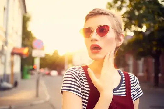 Симпатичная женщина в солнцезащитных очках на прогулке на открытом воздухе, позирует с веселым настроением