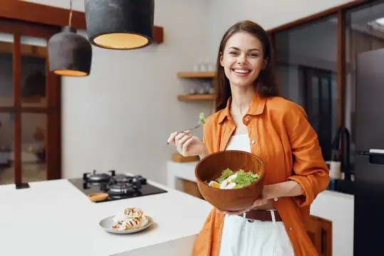 Улыбающаяся девушка с миской салата на светлой кухне