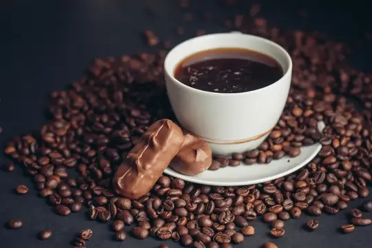 Белая чашка кофе с печеньем на рассыпанных зернах