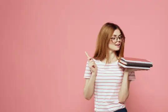 Молодая студентка с книгами на розовом фоне, в очках, крупный план лица