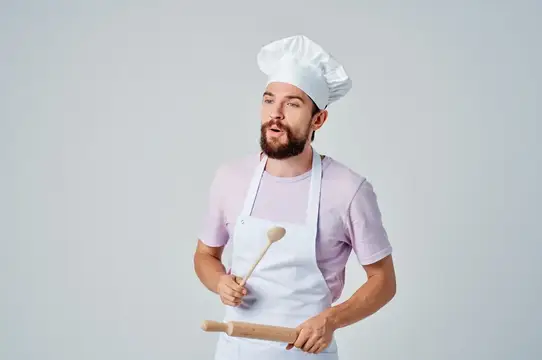 Бородатый мужчина в поварском колпаке и фартуке с половником и скалкой