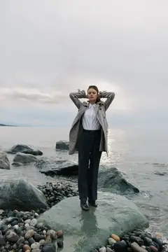 Молодая женщина в деловом костюме стоит на камне у моря