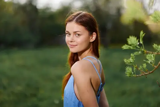 Портрет молодой женщины с красивой улыбкой, демонстрирующей зубы, на фоне деревьев в весенней природе в солнечный день