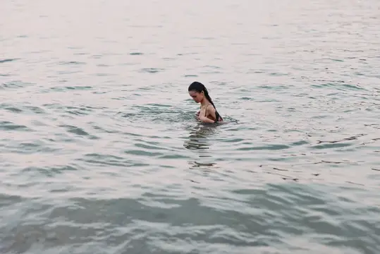 Темноволосая девушка купается в спокойной воде в пасмурный день