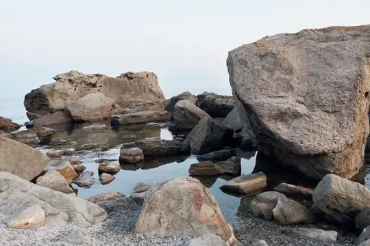 Большие серые камни и тихая вода у скалистого берега