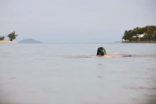 Темноволосая женщина плывёт в спокойной воде в пасмурный день