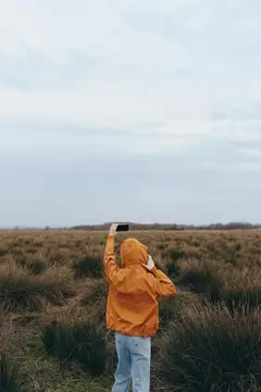 Женщина на открытом воздухе, поле, куртка, толстовка, облачно, природа, стоит непринужденно, женский портрет в оранжевом пальто и синих джинсах, стоит в открытом поле на ветру и в облаках, мягкий свет
