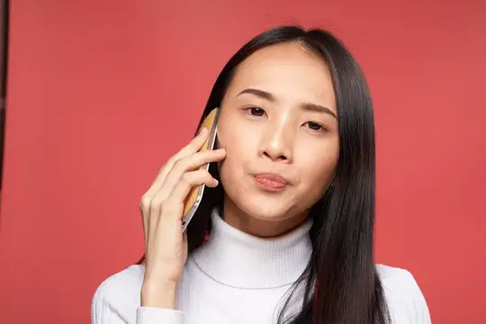 Азиатская девушка с длинными волосами слушает телефон на красном фоне