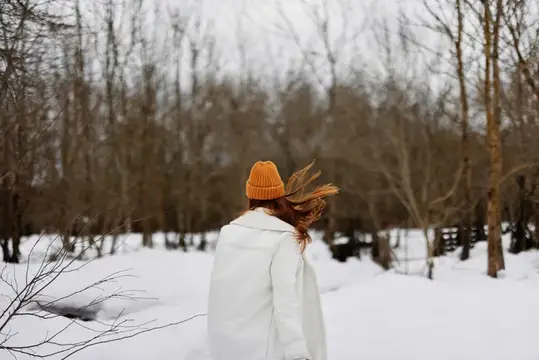 Девушка в оранжевой шапке идёт по зимнему лесу
