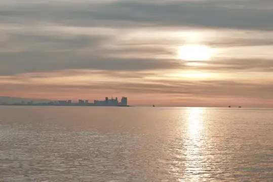 Вечерний свет над морем с удаленным городским силуэтом, мягкие облака и сияющий горизонт