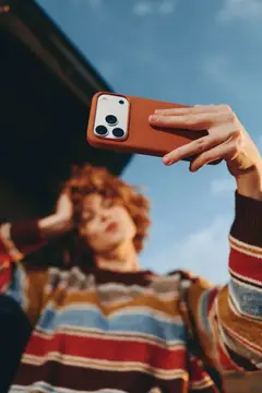 Рыжеволосая девушка делает селфи на смартфон в терракотовом чехле