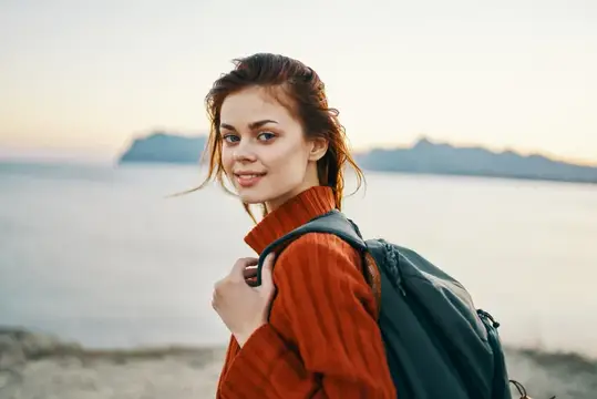 Молодая женщина с рюкзаком улыбается на берегу моря