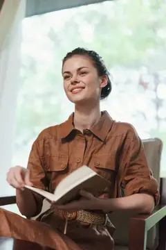 Улыбающаяся темноволосая девушка с книгой у окна
