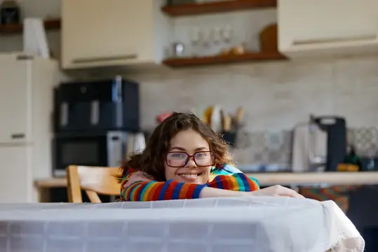 Улыбающаяся девушка в очках лежит на столе на кухне