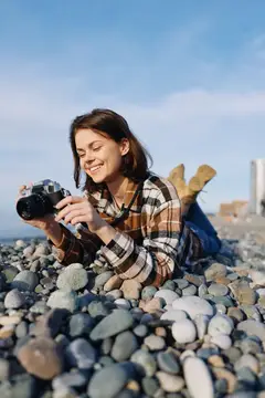 Улыбающаяся девушка лежит на каменистом пляже с фотокамерой