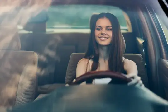 Улыбающаяся темноволосая девушка за рулём автомобиля