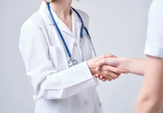 Врач в белом халате со стетоскопом пожимает руку пациенту