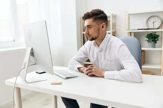 Молодой мужчина в белой рубашке работает за компьютером в светлом офисе
