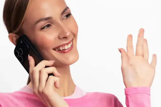 Счастливая женщина в розовом топе со смартфоном в руке машет и улыбается