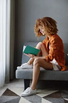 Веселая молодая женщина с радостью читает книгу, сидя на диване в уютной комнате
