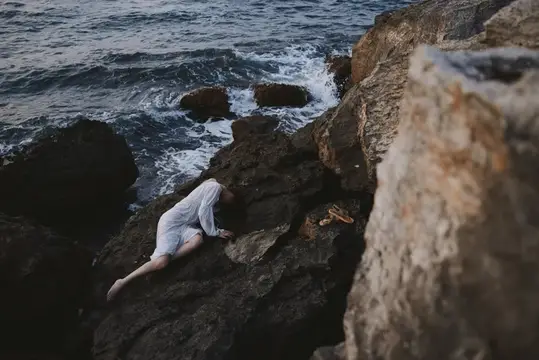 Девушка в белом платье лежит на скалах у бурного моря