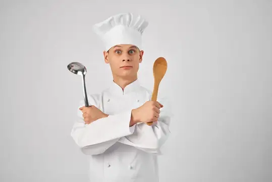 Мужчина в форме шеф-повара работает на кухне ресторана, используя кухонные принадлежности