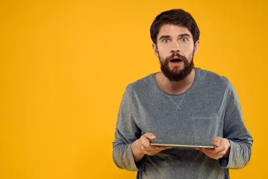 Удивлённый бородатый мужчина с планшетом на жёлтом фоне