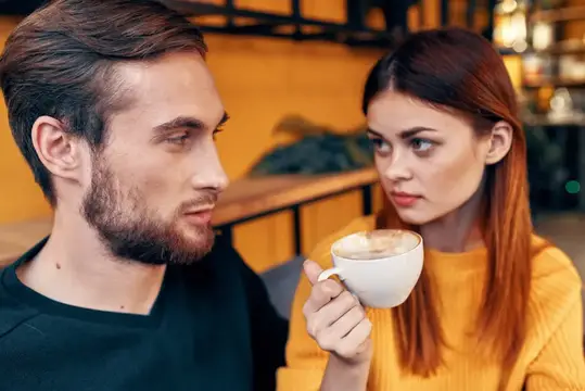 Молодой бородатый мужчина и рыжеволосая девушка с кофе в кафе