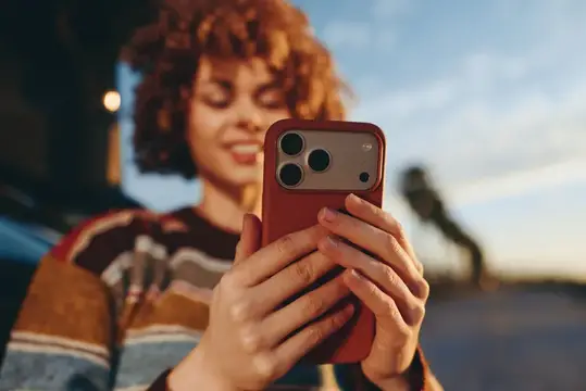Улыбающаяся кудрявая девушка смотрит в смартфон на улице